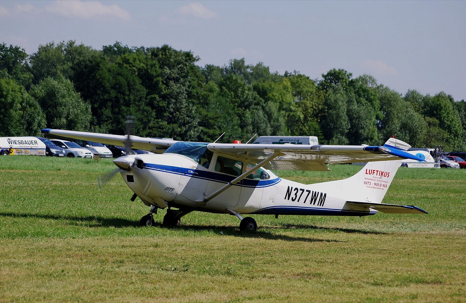 A white and blue Cessna 182 Skylane with its propeller turning on a grass airfield