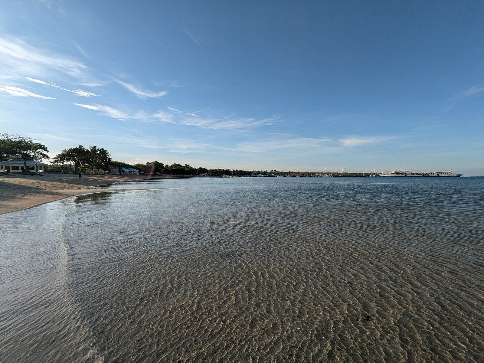 Clear shallow water rippling over the sandbar at Capusan Beach, Cuyo, with the port and a ferry beyond