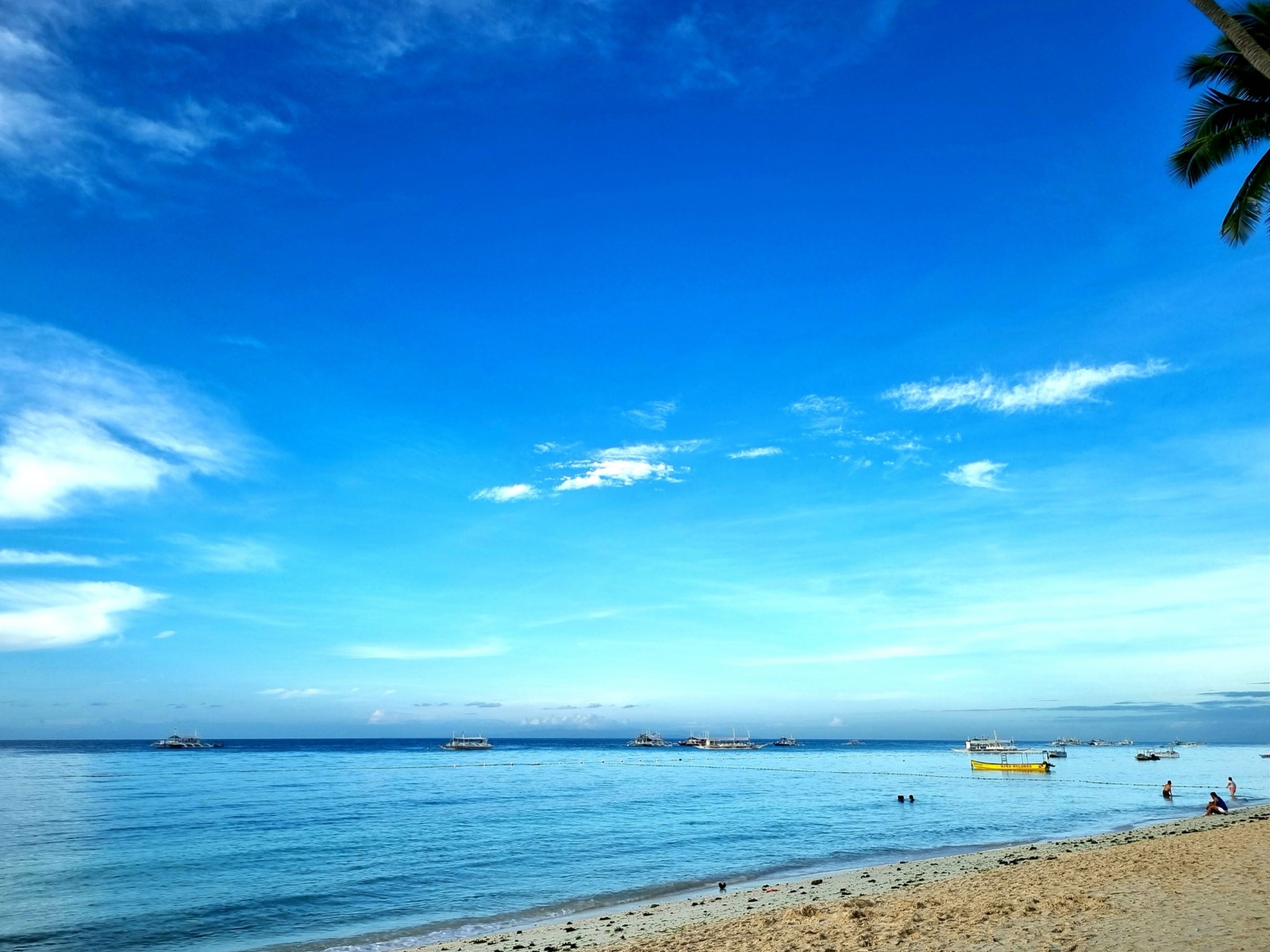 Outrigger boats moored off the sand of Alona Beach on Panglao Island, Bohol, under a clear blue sky