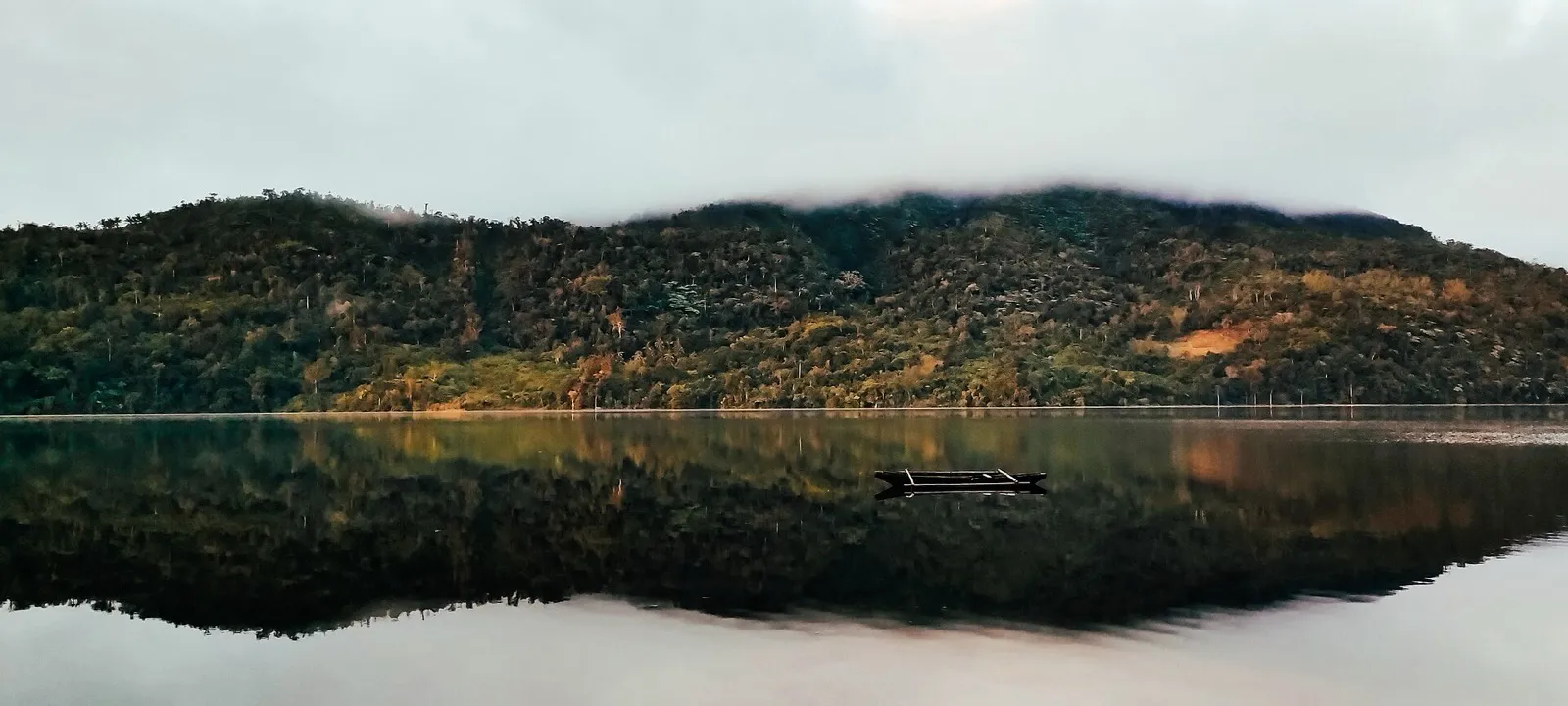 A small boat on the still water of Lake Danao above Ormoc, with forested hills and low cloud reflected below