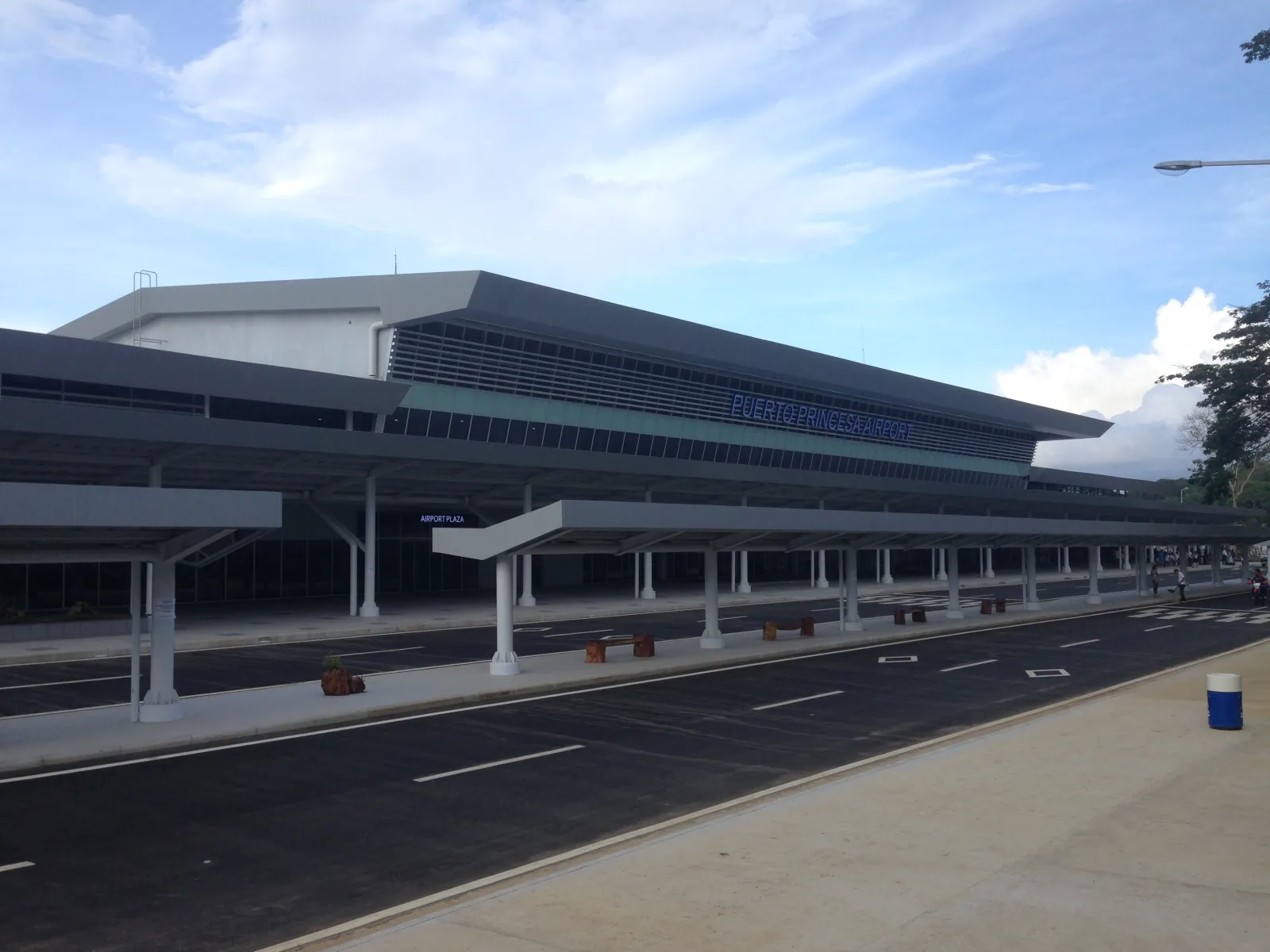 The terminal building of Puerto Princesa International Airport under a partly cloudy sky, empty forecourt in front