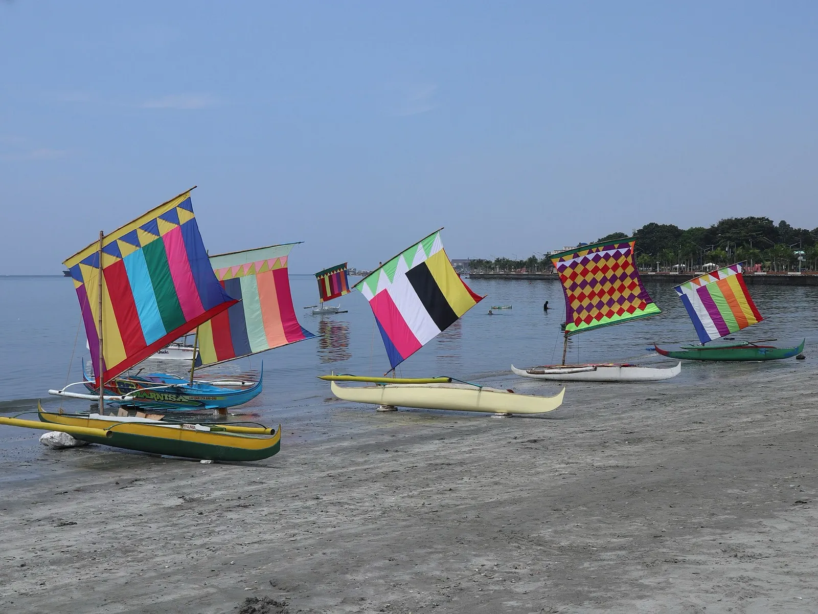 Vinta outrigger boats with brightly striped sails pulled up on the shore in Zamboanga City